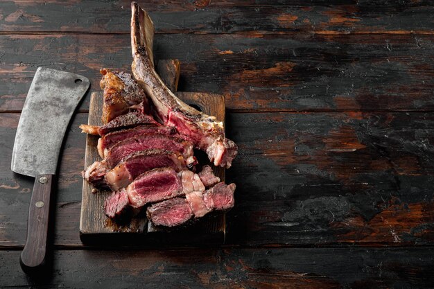 Set di carne mediamente rara Tomahawk marmorizzata a secco invecchiata alla griglia di manzo, su tavola da portata in legno, su vecchio sfondo tavolo in legno scuro, con copia spazio per il testo