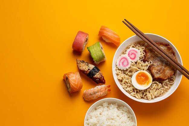 Set di cibo tradizionale giapponese: ramen di zuppa calda, riso bianco bollito, sushi, panini su sfondo arancione brillante. Piatti della cucina giapponese, dall'alto, cena asiatica o modello di pranzo, spazio per il testo