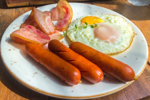 Set di colazione americana con pancetta, uova fritte e salsiccia sul fondo della tavola di legno