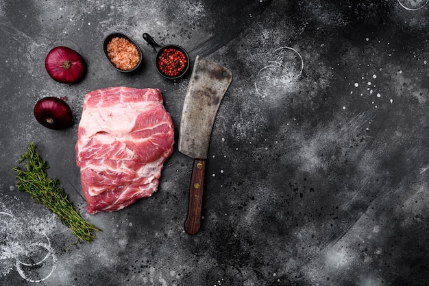Set di collo crudo di carne di maiale, con ingredienti ed erbe aromatiche, con vecchio coltello da macellaio, su sfondo nero tavolo in pietra scura, vista dall'alto piatta, con spazio copia per il testo