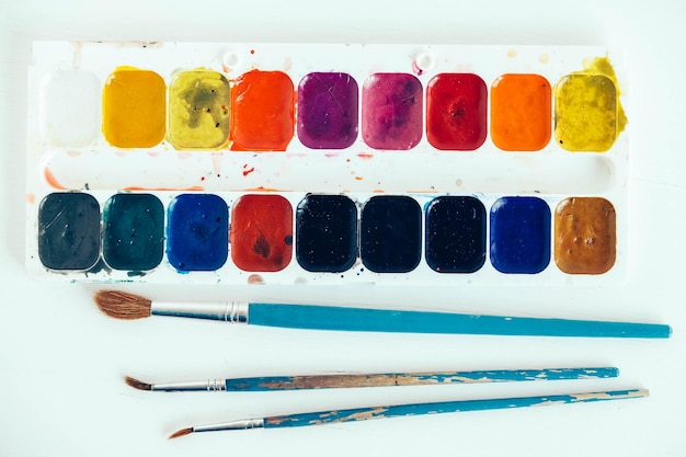 Set di colori ad acquerello e pennelli per dipingere su sfondo bianco. Vista dall'alto. Copia, spazio vuoto per il testo