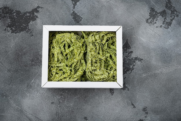 Set di confezioni di pasta verde di tagliatelle, su sfondo di tavolo in pietra grigia, vista dall'alto piatta, con spazio di copia per il testo