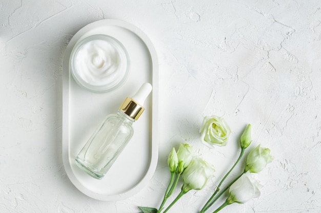 Set di cosmetici naturali per la cura della pelle antietà su vassoio bianco con fiori di eustoma Olio essenziale per il viso di bellezza e crema per il viso in una confezione di vetro senza marchio