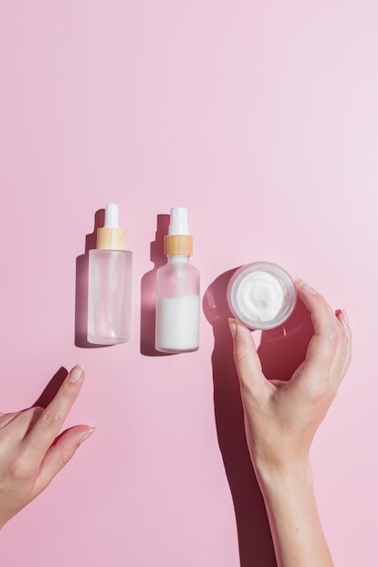 Set di cosmetici per la cura della pelle Foutine in tre fasi per una pelle sana Mano femminile che sceglie un vasetto di crema o una bottiglia con essenza Sfondo rosa Contenitori mockup