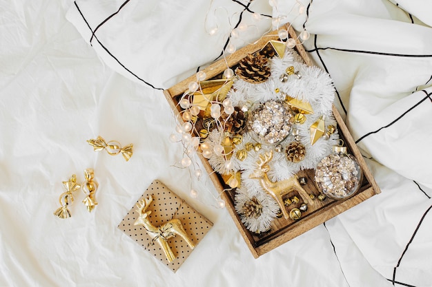 Set di decorazioni natalizie e regalo in scatola di legno sul letto bianco con una coperta. Concetto di vacanza. Disposizione piatta, vista dall'alto