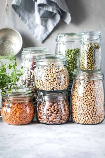 Set di diversi legumi in barattoli di vetro su, tavolo bianco concreto. Una fonte di proteine per i vegetariani. Il concetto di alimentazione sana e conservazione degli alimenti.