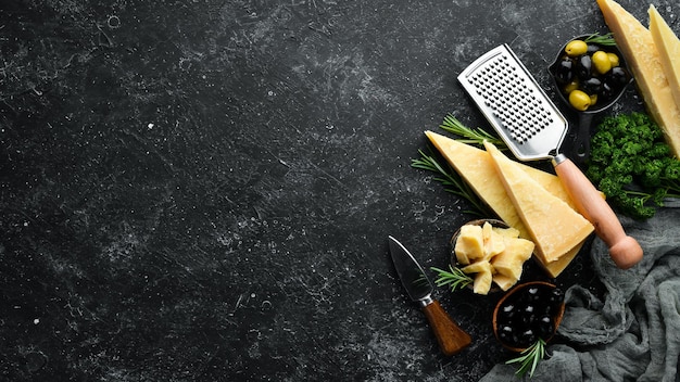 Set di formaggi a pasta dura con coltelli da formaggio su sfondo di pietra nera. Parmigiano. Vista dall'alto. Spazio libero per il tuo testo.