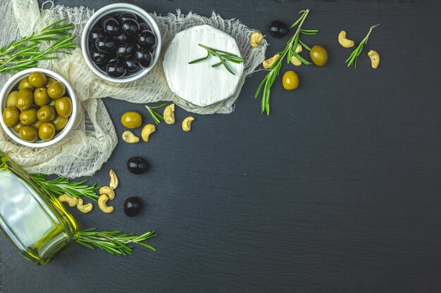 Set di formaggio camembert olive nere e verdi uova di quaglia su piatti olio d'oliva e rosmarino su uno sfondo di tavolo in pietra nera Vista dall'alto spazio copia