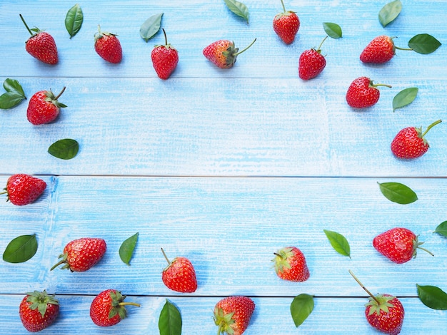 Set di fragole rosse e foglie verdi su fondo di legno blu con lo spazio della copia. Frutto succoso.