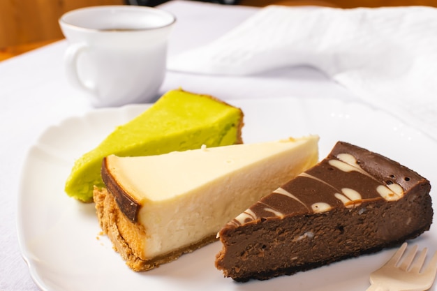 Set di New York, cioccolato e cheesecake al pistacchio su piatto bianco e tazza di caffè. Avvicinamento.