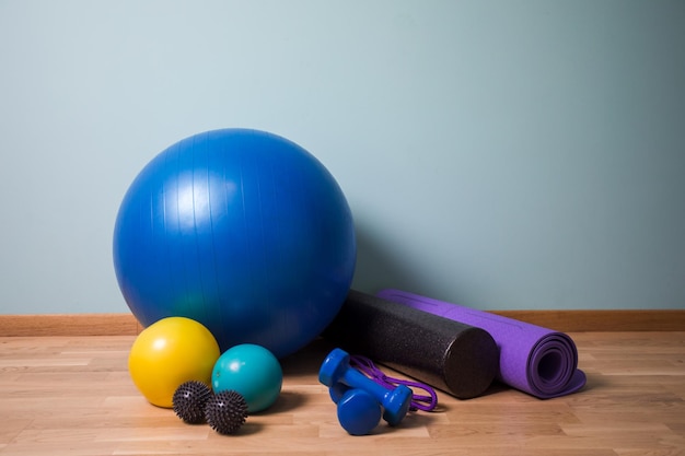 Set di palline di diverse dimensioni rotolo di schiuma e tappetino yoga su pavimento in legno Attrezzatura professionale per fitness e rilascio miofasciale