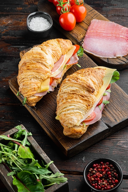 Set di panini croissant BLT classici, con erbe e ingredienti, sul vecchio fondo della tavola in legno scuro