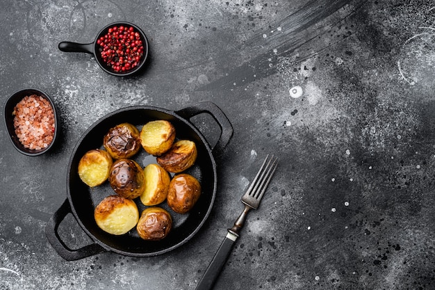 Set di patate al forno, in padella in ghisa, su sfondo nero tavolo in pietra scura, vista dall'alto piatta, con spazio copia per il testo