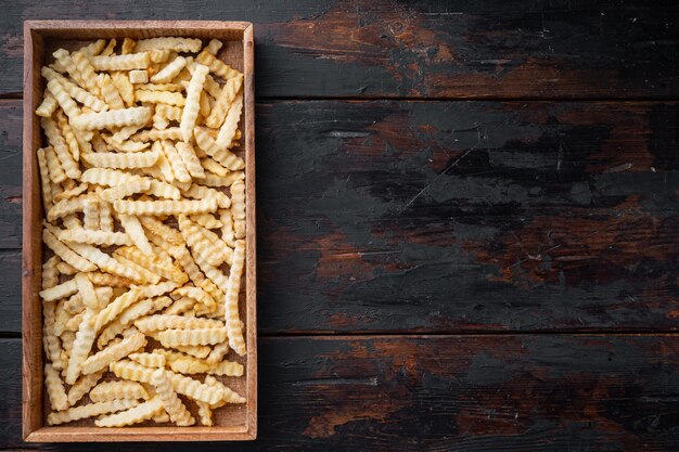 Set di patatine fritte congelate crinkle, in una scatola di legno, sul vecchio tavolo in legno scuro, vista dall'alto piatto lay