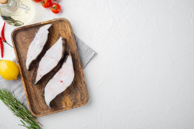 Set di pesce halibut affettato, con ingredienti ed erbe di rosmarino, su sfondo di tavolo in pietra bianca, vista dall'alto piatta, con copia spazio per il testo