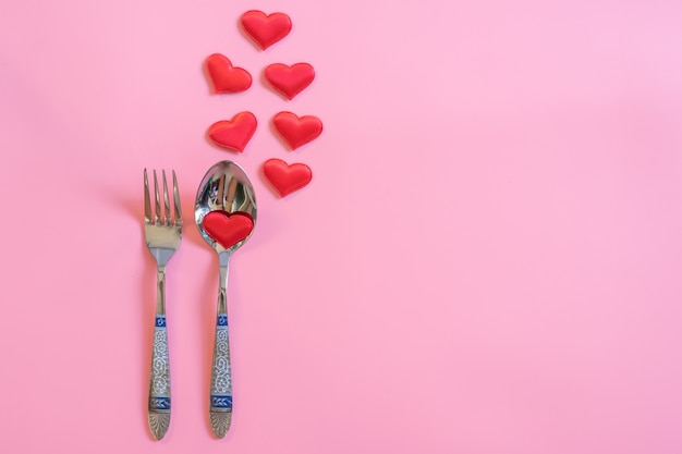 Set di posate e cuore rosso su colore pastello rosa con spazio per il testo.