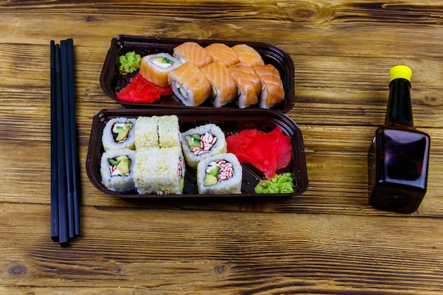 Set di rotoli di sushi in scatole di plastica salsa di soia e bacchette sulla tavola di legno