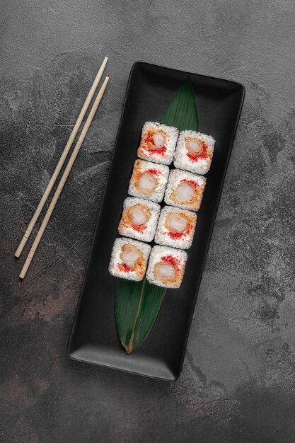 Set di rotoli quadrati di maki con caviale di shrim tigre e foglia di bambù verde in un piatto di ceramica nera con bacchette su uno sfondo grigio scuro con texture vista dall'alto