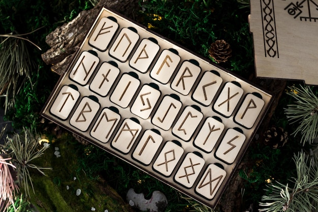 Set di rune di legno in una scatola giacciono sul muschio nella foresta. piattaforme rettangolari di legno su cui sono scolpite rune scandinave giacciono su muschio verde circondato da sale, coni, aghi di abete e corteccia