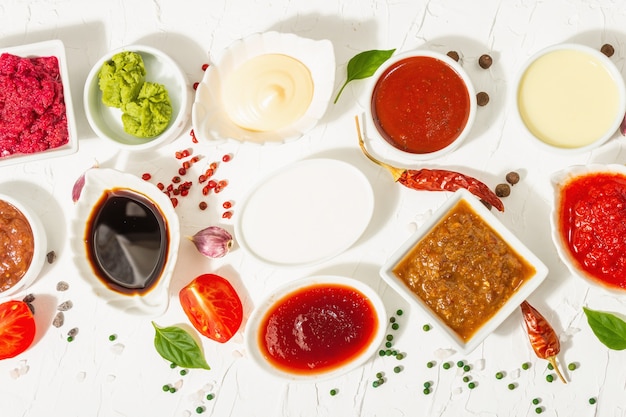 Set di salse diverse: ketchup, maionese, barbecue, soia, chutney, wasabi, adjika, rafano, aioli, marinara. Luce dura alla moda, ombra scura. Sfondo bianco stucco, vista dall'alto