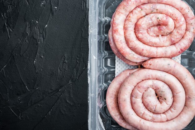 Set di salsiccia di carne di maiale a spirale, sulla tavola nera, in confezione di plastica, vista dall'alto piatto laico, copyspace