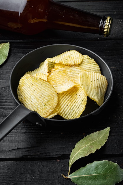 Set di snack salati con patatine e bottiglia di birra, su legno nero