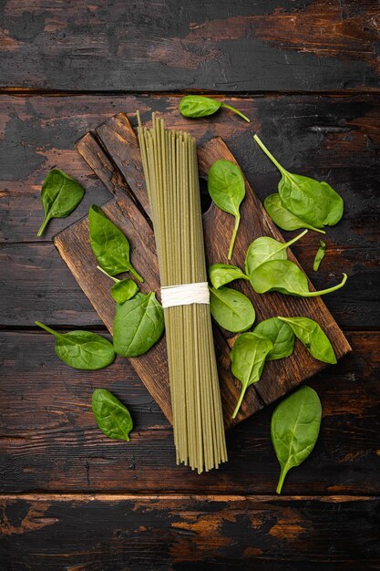 Set di spaghetti di pasta verde italiana cruda, su vecchio sfondo di tavolo in legno scuro, vista dall'alto piatta