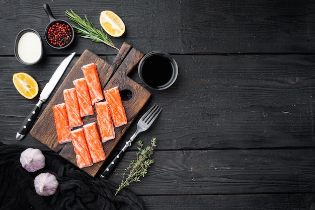 Set di surimi di bastoncino di carne di granchio fresca, sul tagliere di legno, sul fondo della tavola in legno nero, vista dall'alto laici piatta, con copyspace e spazio per il testo