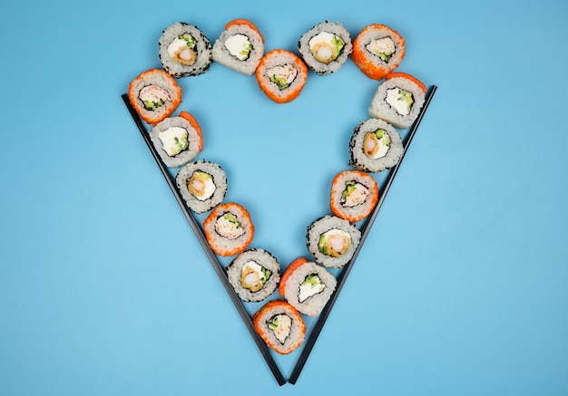 Set di sushi e panini con bastoncini serviti come cuore su sfondo blu