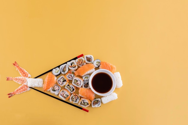 set di sushi e salsa di soia su un piatto bianco a forma di pesce pronto da mangiare su sfondo giallo