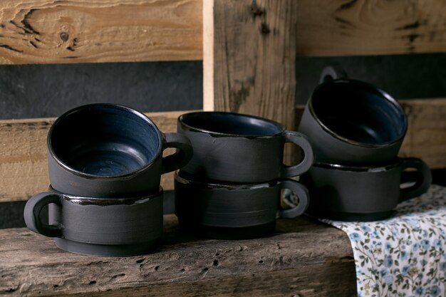 Set di tazze da tè vuote in ceramica nera opaca artigianale in piedi su ripiano in legno Interni rustici
