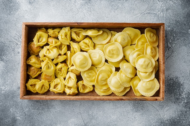 Set di tortellini e ravioli fatti a mano crudo italiano, in una scatola di legno, sul tavolo grigio, vista dall'alto laici piatta