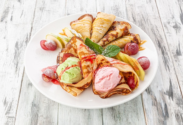 Set di tradizionali frittelle russe dolci. Con topping e gelato. In un piatto bianco. Fondo in legno chiaro. Vista dall'alto.