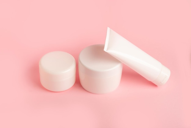 Set di tre scatole di plastica bianche pulite con crema per il corpo su sfondo rosa