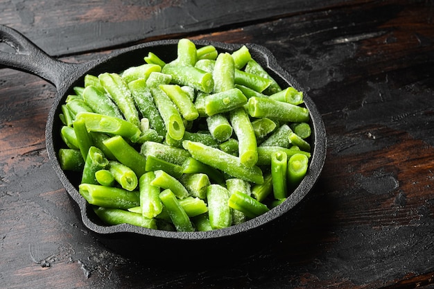 Set di verdure di fagiolini tagliati congelati, in padella in ghisa, su un vecchio tavolo di legno scuro