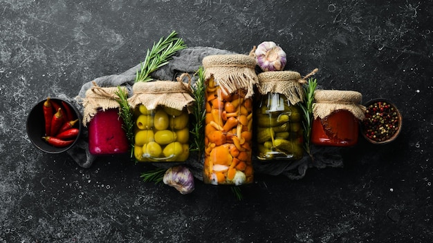Set di verdure in scatola e funghi in vasetti di vetro Set di cibo in salamoia su sfondo di pietra nera Vista dall'alto