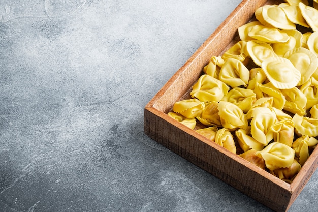 Set tortellini e ravioli crudi italiani fatti a mano, in scatola di legno, sul tavolo grigio
