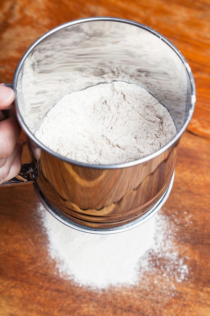 Setacciare la farina attraverso un setaccio sul tavolo di legno