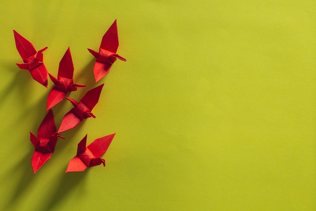 Sette uccelli origami rossi stanno volando guidati da un uccello rosa, isolato su bianco, gru di carta origami rossa