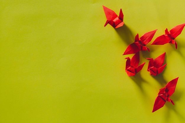 Sette uccelli origami rossi stanno volando guidati da un uccello rosa isolato su biancoGru di carta origami rossa
