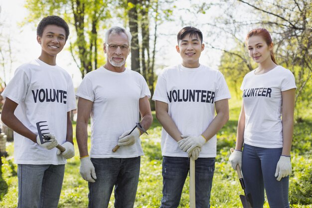 Settore ambientale. Energici quattro volontari in piedi e con in mano attrezzi da giardino