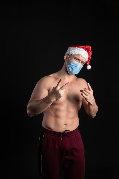 Sexy Babbo Natale Fitness bitseps mostra addominali cubi un atleta con una bella figura su sfondo nero In un berretto rosso durante le vacanze di Natale con labbra tenere