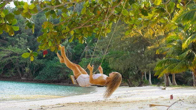 Sexy donna calda sta oscillando su un'altalena Ragazza cattiva erotica in posa sulla spiaggia sullo sfondo del mare Concetto bellezza naturale corpo femminilità e sessualità dissolutezza e coraggio