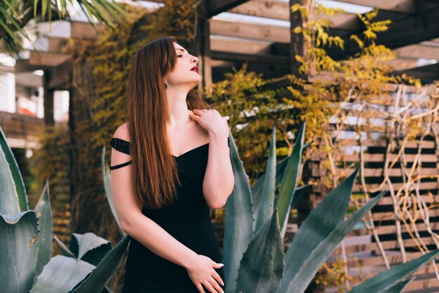 Sexy donna ricca dai capelli lunghi in un vestito nero che riposa nel suo giardino, rilassante