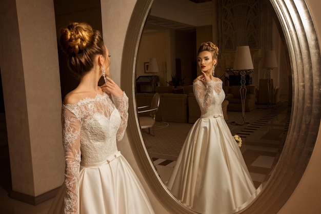 Sexy giovane sposa bionda in abito da sposa guardando allo specchio