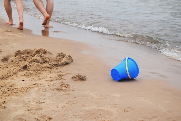 Sezione bassa di persone che camminano con un secchio blu sulla riva alla spiaggia