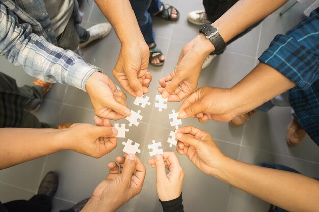 Sezione bassa di persone che tengono pezzi di puzzle in piedi sul pavimento in piastrelle