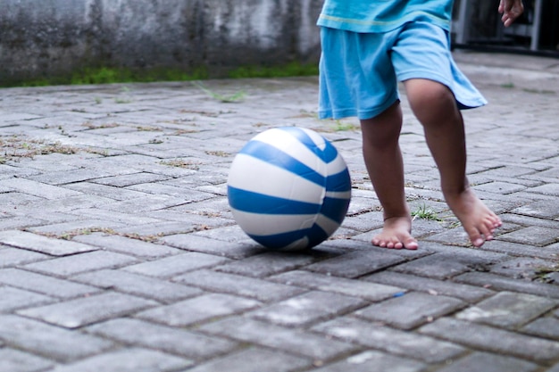 Sezione bassa di un bambino che gioca con la palla sul marciapiede