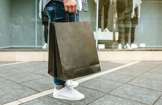 Sezione bassa di un giovane irriconoscibile che fa shopping con sacchetti di carta in mano