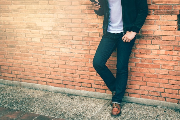 Sezione bassa di un uomo che usa il telefono mentre è in piedi contro un muro di mattoni